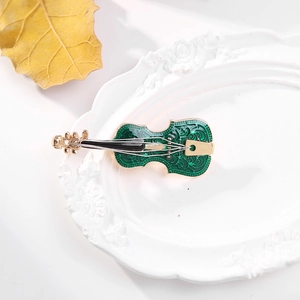 Vintage green enamel violin brooch with golden scrollwork on a white ceramic tray