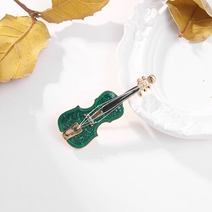 Detail of a green enamel violin brooch with golden edges on a white ceramic plate