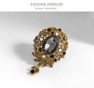 Detail of vintage gold-plated brooch featuring a grey faceted crystal and black pendant