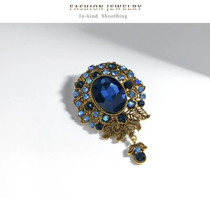 Detail of vintage gold brooch featuring a deep blue oval sapphire and teardrop pendant