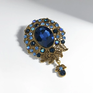 Vintage gold brooch featuring a deep blue oval stone surrounded by crystal rhinestones