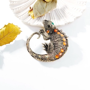 Vintage gold lizard brooch with orange gemstones and green eye on a white shell plate