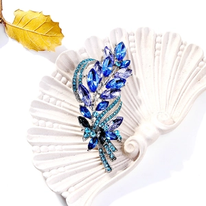 Detailed leaf brooch with blue rhinestones on a white shell-shaped display tray
