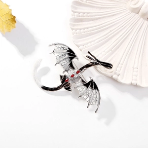 Broche dragon gothique noire et argentée avec pierres rouges sur un plateau coquillage