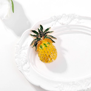 Détail d'une broche ananas en émail jaune avec strass verts sur une plaque blanche