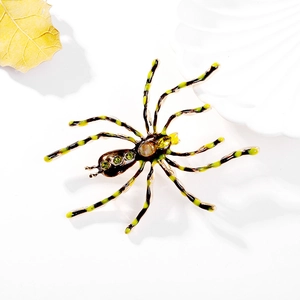 Vintage spider brooch with green rhinestones and striped legs on a white background