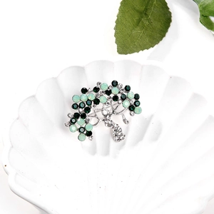 Silver tree brooch with green crystals and rhinestones on a white shell tray