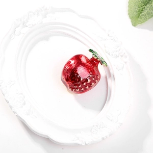 Detail of red apple brooch with green leaf on a decorative white ceramic tray