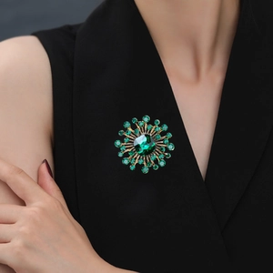 Elegant gold-tone sunburst brooch with emerald green crystals on a black blazer
