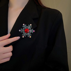 Snowflake brooch with red center stone and green rhinestones on black suit jacket