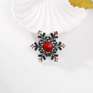 Sparkling snowflake brooch with red and green crystals on a white ceramic dish
