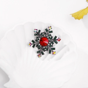 Macro shot of snowflake brooch with red gemstone and green crystals on white plate