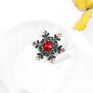 Snowflake brooch with red center stone and green rhinestones on a white shell tray