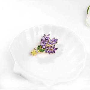 Dettaglio macro della spilla lavanda con cristalli viola e foglie d'oro su vassoio