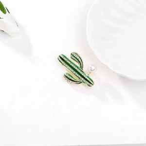 Dettaglio spilla a forma di cactus con smalto verde, cristalli e perla su sfondo bianco