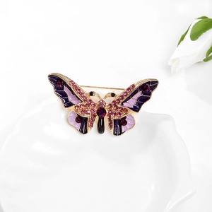 Détail de la broche papillon en émail violet et strass sur un plat en céramique blanc