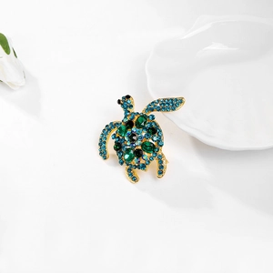 Detailopname van gouden schildpadbroche met blauwe en groene strassteentjes op wit