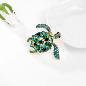 Charmante gouden schildpad broche met blauwe en smaragdgroene kristallen op wit keramiek