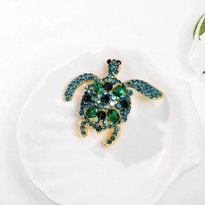 Prachtige gouden schildpadbroche met blauwe en groene strass in een witte schelpschaal