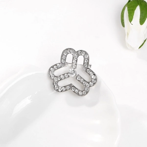 Close-up of a silver clover brooch with sparkling rhinestones on a white ceramic surface