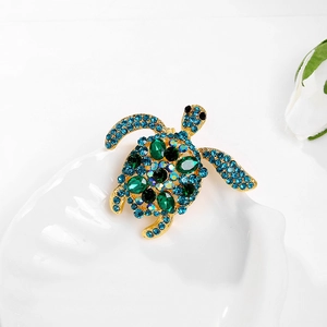 Detailopname van een gouden schildpad broche met blauwe strassteentjes en groene kristallen
