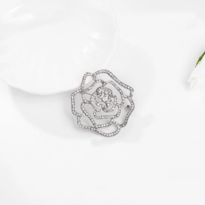 Élégante broche rose argentée avec strass blancs et pétales ajourés sur fond blanc