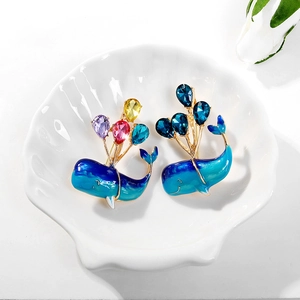 Close-up of enamel whale balloon brooches with sparkling crystals on a shell dish