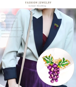 Detailansicht einer lila Traubenbrosche mit grünen Emailleblättern an einem Blazer