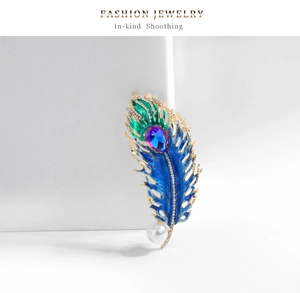 Macro detail of a peacock feather brooch with blue enamel, crystals and a white pearl