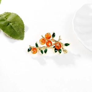 Dettaglio macro della spilla ramo di cachi con frutti arancioni e foglie smaltate verdi