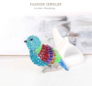 Dettaglio spilla a forma di uccello colorato con strass blu su supporto bianco