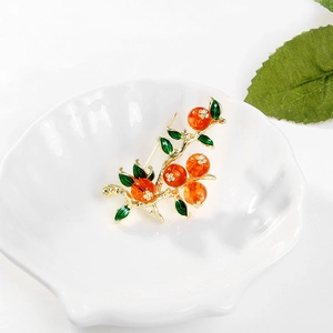 Dettaglio spilla cachi vintage con perline arancioni e foglie verdi su piatto guscio