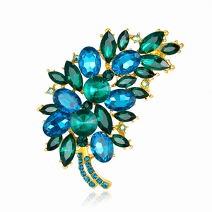 Elegant floral brooch with blue and green gemstones on a gold finish metal base