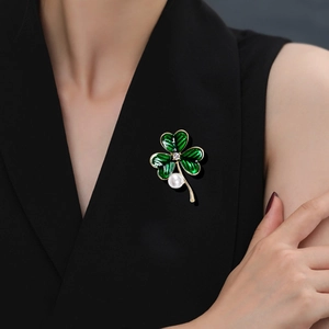 Élégante broche trèfle en émail vert avec perle blanche sur fond de tissu noir