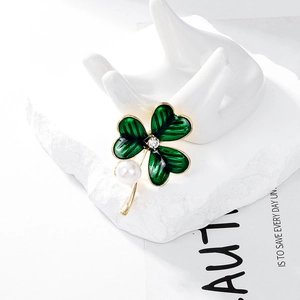 Détail d'une broche trèfle en émail vert avec perle et cristal sur un support blanc