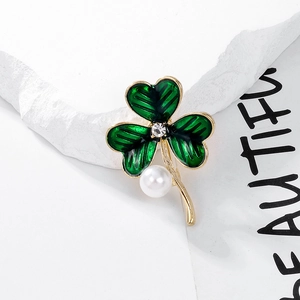 Vue macro de broche trèfle en émail vert avec perle blanche et pétales dorés texturés