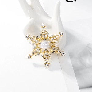 Detalle de un broche de copo de nieve dorado con diamantes de imitación y una perla