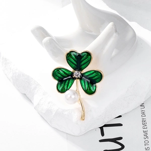 Détail d'une broche trèfle en émail vert avec perle blanche sur un support décoratif