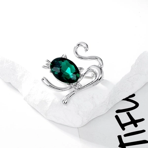 Detailed view of cat brooch with a large faceted green crystal on stone background