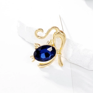 Detail of gold cat brooch featuring a large oval dark blue crystal on white stone