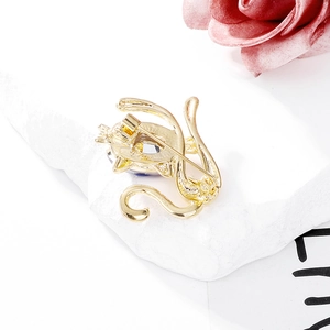 Cute golden cat brooch with dark blue crystal drop on white stone background
