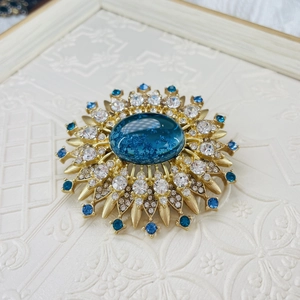 Vintage gold sunflower brooch featuring a large blue gemstone with crystal accents