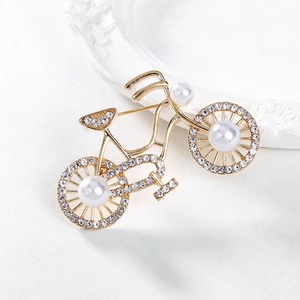 Spilla bici dorata elegante con strass bianchi e perle su sfondo bianco tramato