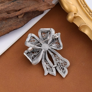 Broche nœud vintage en argent avec filigrane et strass sur un socle texturé élégant