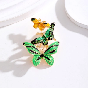 Enameled butterfly brooch with green rhinestones and gold plating on a white stand