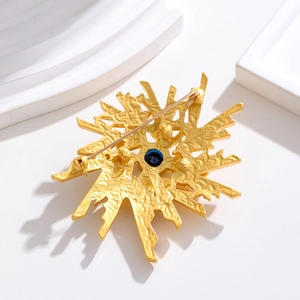 Vintage gold brooch with sunburst texture and blue gemstone in a retro artistic design