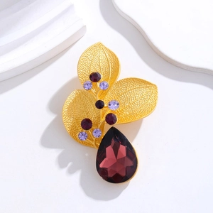 Macro detail of golden leaf brooch with purple rhinestones and red teardrop gem