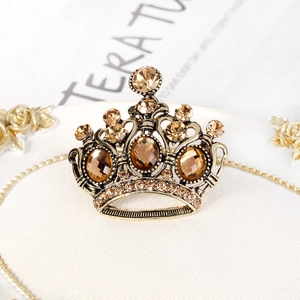 Spilla a corona vintage in oro con cristalli champagne e strass su sfondo bianco