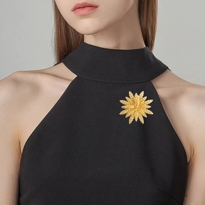 Elegant gold sunburst wheat brooch on black dress with textured metal starburst design