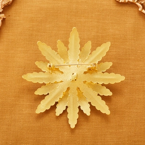 Golden sunburst brooch with matte textured back and secure pin clasp on orange fabric
